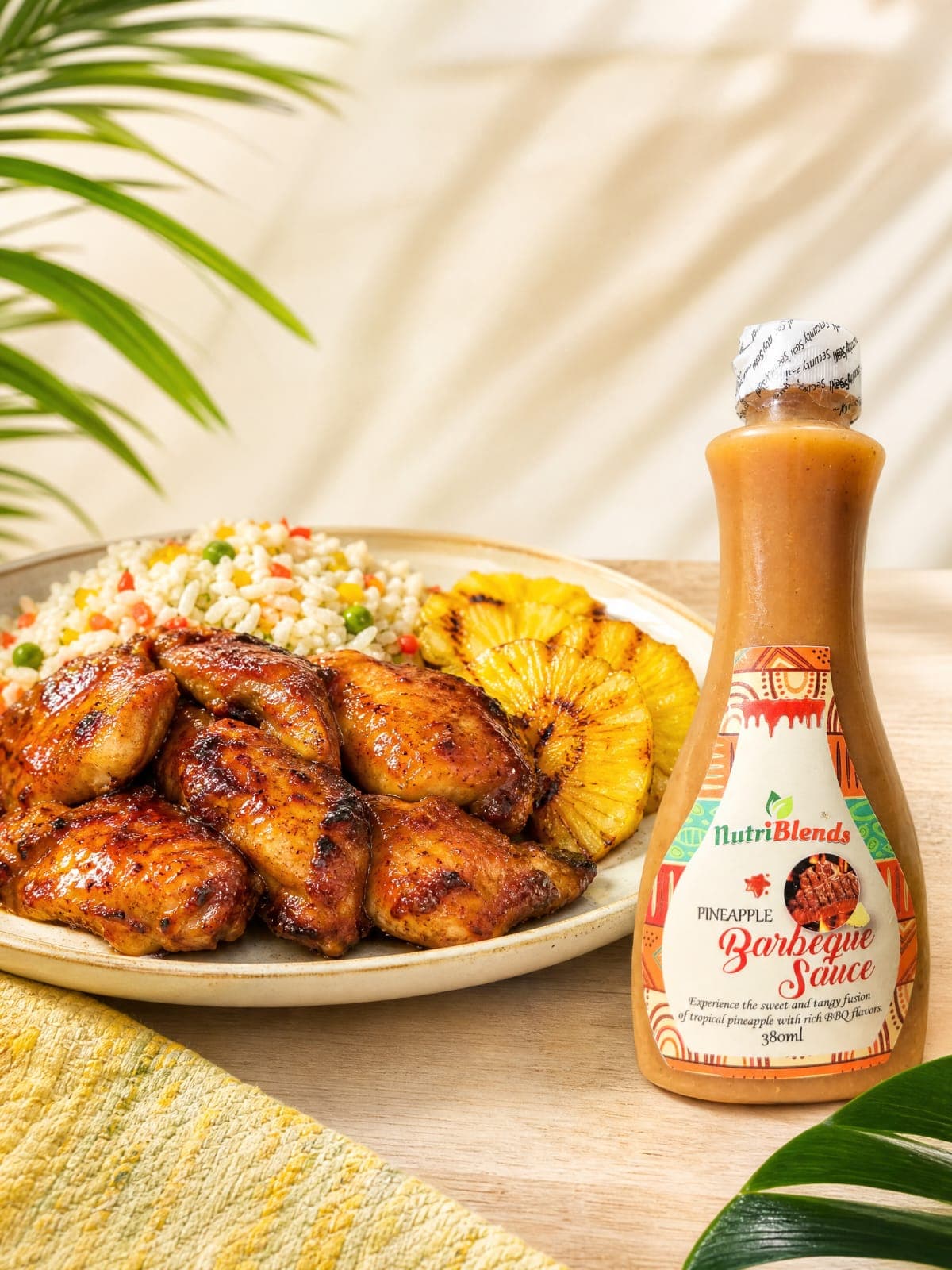 Plate of pineapple BBQ glazed chicken with colourful rice and grilled pineapple beside a bottle of Nutriblends Pineapple Barbeque Sauce.